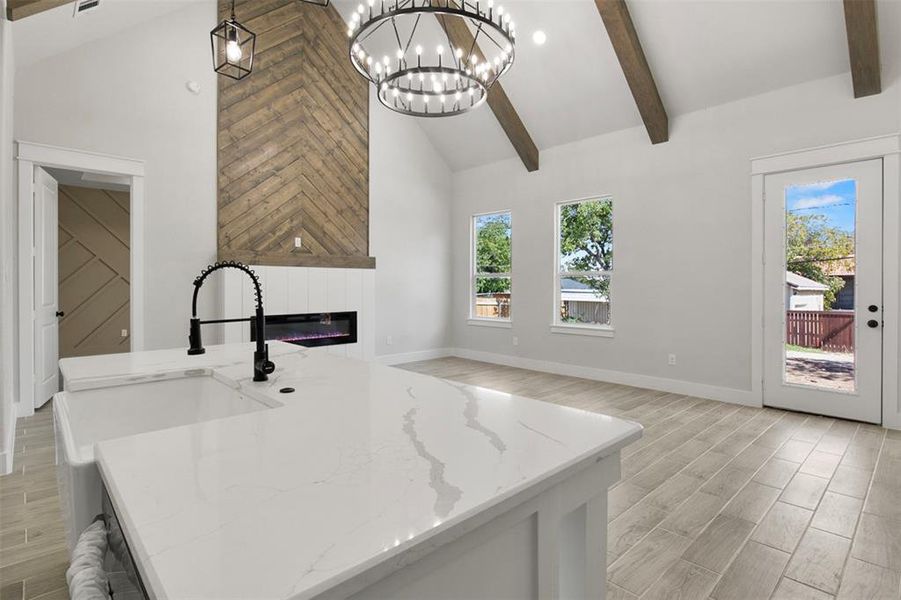 Kitchen with light stone countertops, a center island with sink, hanging light fixtures, and a healthy amount of sunlight