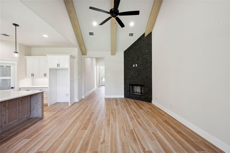 Unfurnished living room with beamed ceiling, ceiling fan, light wood-type flooring, and a fireplace