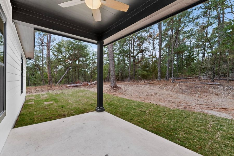 Covered concrete patio featuring a ceiling fan, black support column, and an expansive natural wooded backdrop Covered concrete patio featuring a ceiling fan, black support column, and an expansive natural wooded backdrop