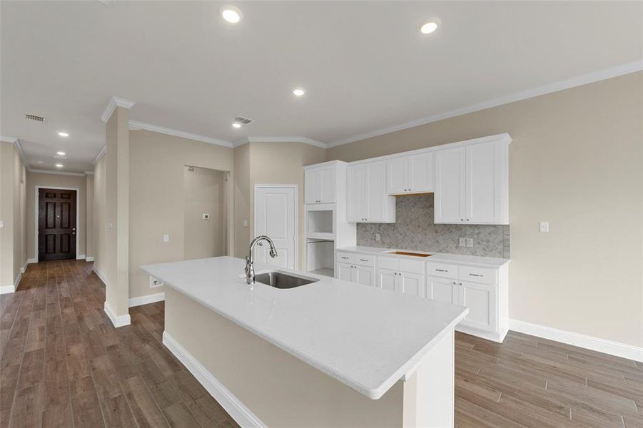 Bright kitchen featuring white cabinetry, a large center island with an undermount sink, quartz countertops, a tiled backsplash, and recessed lighting