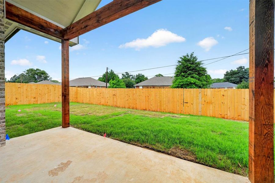 Covered concrete patio featuring exposed wood beams, a spacious lawn, and a privacy fence