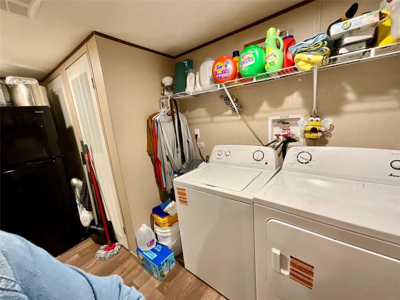 Dedicated laundry area featuring a white top-load washer and dryer set, wire shelving, and wood-finish flooring