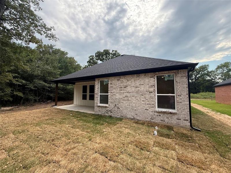 Rear view of house featuring a patio, a lawn, roof with shingles, and brick siding Rear view of house featuring a patio, a lawn, roof with shingles, and brick siding