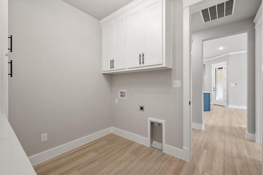 Laundry area featuring white shaker-style cabinetry with black hardware, light wood-finish flooring, and light gray walls