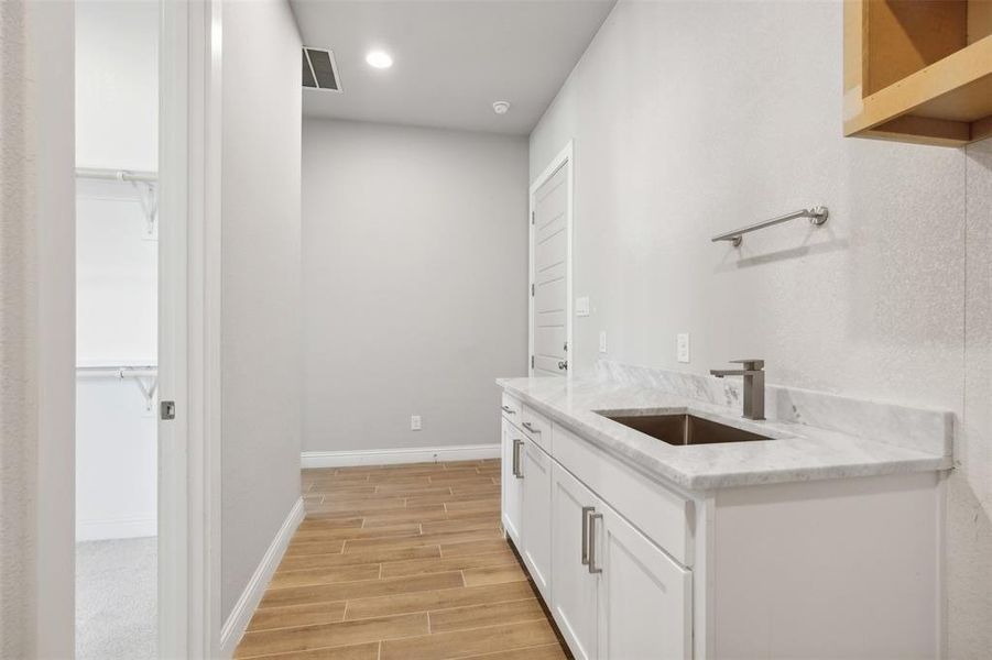 Bar with white cabinetry, light wood-type flooring, light stone countertops, and sink