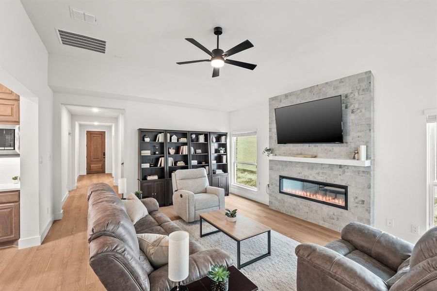 Living room with a stone fireplace, light wood-style flooring, and ceiling fan Living room with a stone fireplace, light wood-style flooring, and ceiling fan