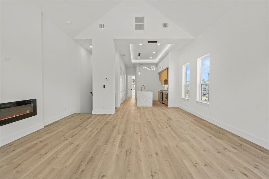 Unfurnished living room with a high ceiling, light wood finished floors, a glass covered fireplace, and recessed lighting