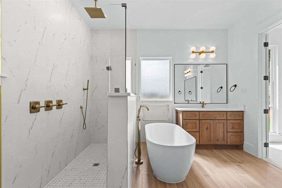 Full bath featuring vanity, a freestanding bath, a marble finish shower, and light wood-style floors