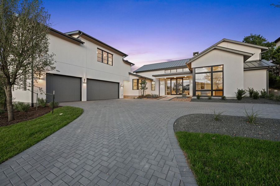 The striking front elevation seamlessly integrates natural textures with clean lines, complemented by a three-car side-entry garage