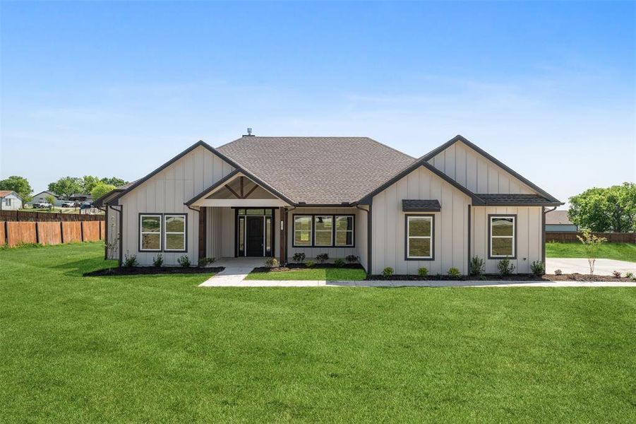 Modern inspired farmhouse with board and batten siding, a front lawn, fence, and roof with shingles