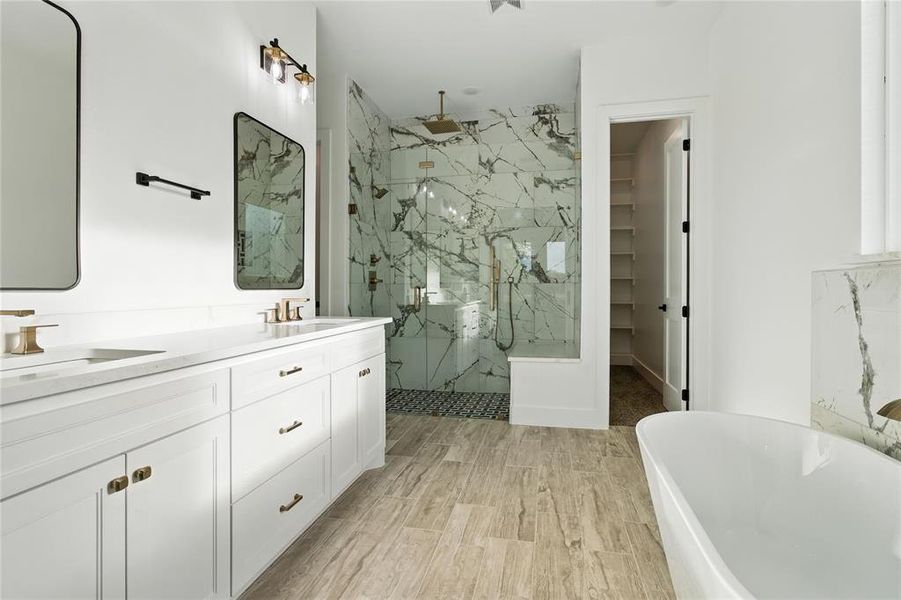 Full bathroom featuring a marble finish shower, a soaking tub, double vanity, wood finished floors, and a spacious closet