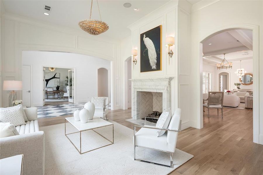 Living room with light hardwood / wood-style floors, a notable chandelier, beamed ceiling, and a high end fireplace