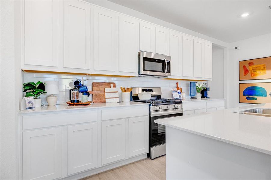 Kitchen with stainless steel appliances, light countertops, backsplash, and white cabinetry