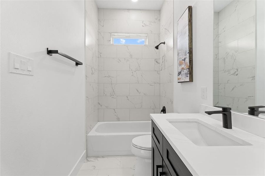 Contemporary bathroom featuring a white soaking tub with a shower, white marble-look tile surround, black vanity with a white countertop and integrated sink, and matte black fixtures