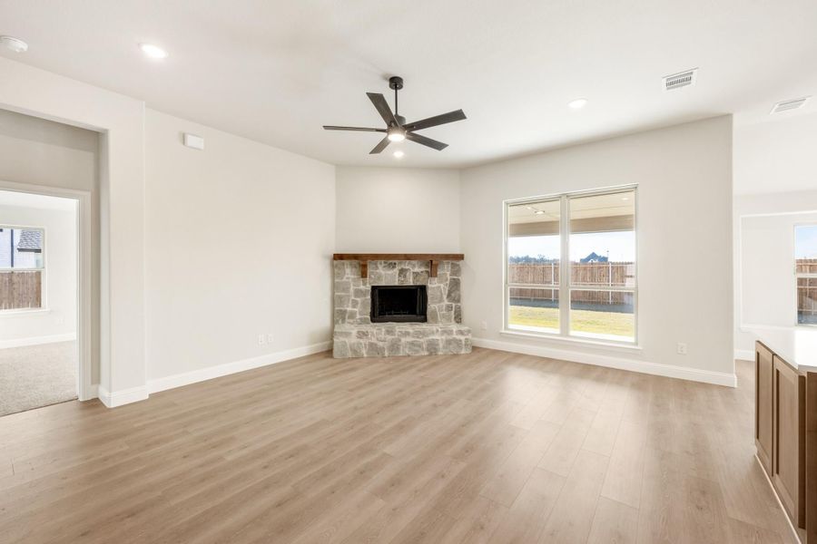 Open living room with stone corner fireplace, wood mantel, ceiling fan, and light hardwood floors