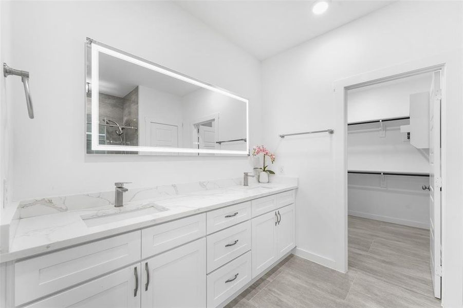 Dual vanity with integrated sinks and white cabinetry, complemented by a large back-lit mirror