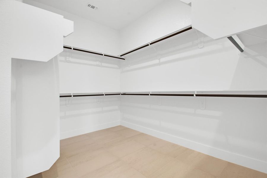 One of two spacious walk-in closets in Primary Room with light tile patterned floors