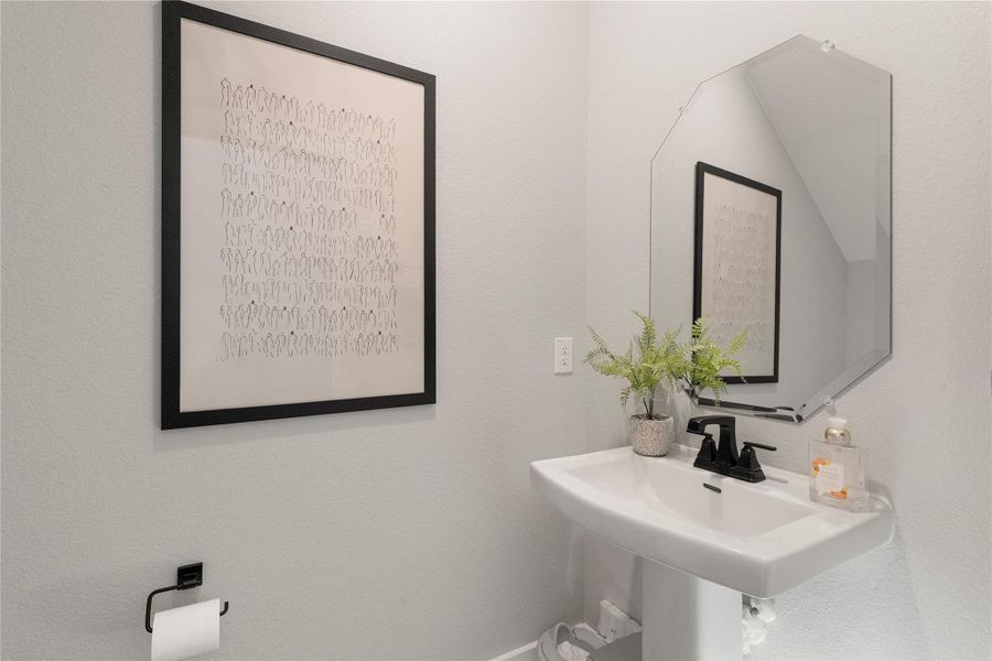 A sleek pedestal sink and frameless mirror elevate this compact powder room. A sleek pedestal sink and frameless mirror elevate this compact powder room.