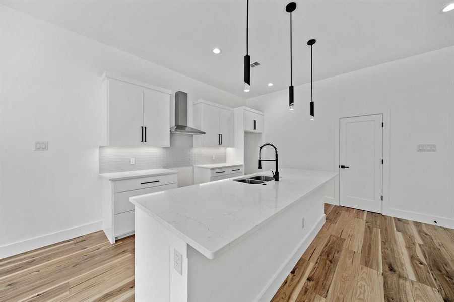 Kitchen with sink, wall chimney exhaust hood, decorative light fixtures, white cabinets, and a center island with sink