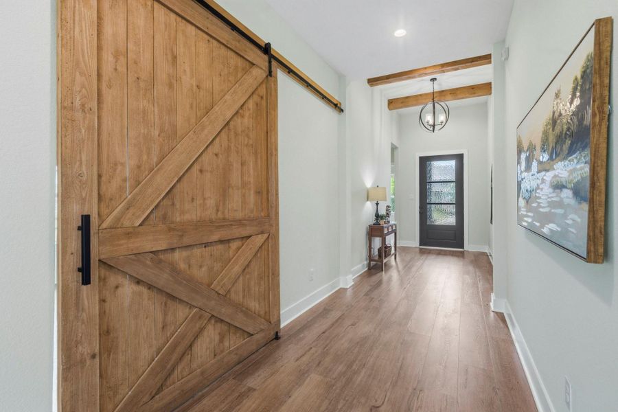 The Foyer, illuminated by an elegant wrought iron orb pendant light, offers a welcoming and spacious introduction to the home, with ample room for a bench seat, storage piece, or coat rack. A large, stately barn door serves as a striking architectural feature, creating a dramatic and sophisticated entrance to the Home Office while adding warmth and character to the space.