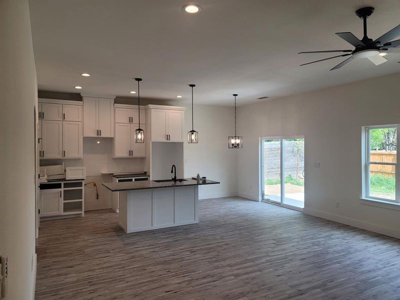 Kitchen featuring white cabinetry, dark wood-style flooring, a kitchen island with sink, ceiling fan, and hanging light fixtures