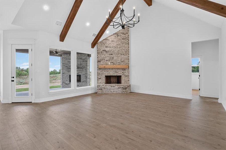Spacious room featuring vaulted ceilings with exposed wood beams, a brick fireplace with a wood mantle, and wood-finish flooring Spacious room featuring vaulted ceilings with exposed wood beams, a brick fireplace with a wood mantle, and wood-finish flooring