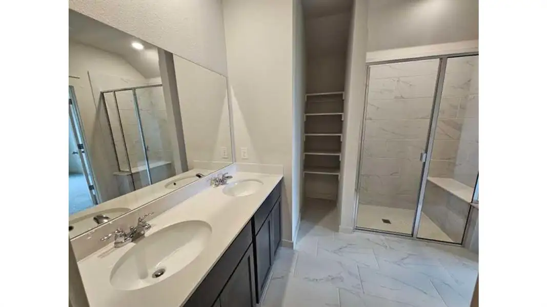 Bathroom featuring a dual vanity with undermount sinks, a spacious walk-in shower with a built-in bench, and integrated shelving
