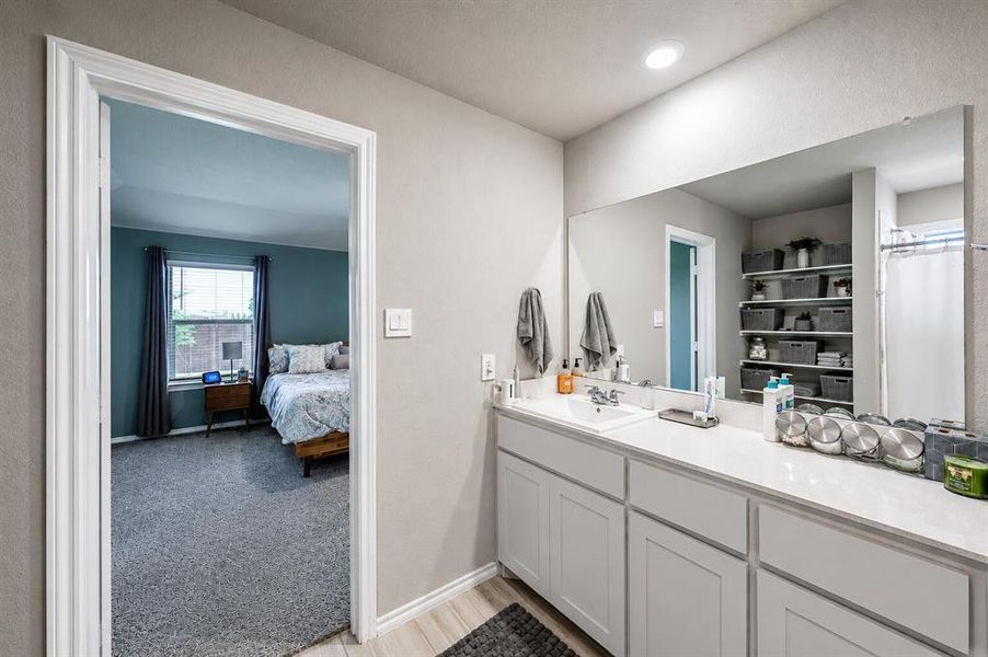 Bathroom featuring an extended vanity with white cabinetry, a single basin sink, and a large wall-mounted mirror
