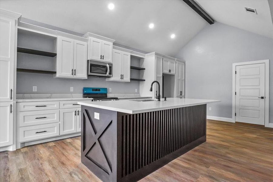 Kitchen with beam ceiling, white cabinetry, sink, a center island with sink, and range