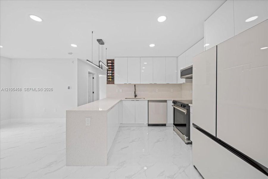 Sleek kitchen featuring white high-gloss cabinetry, stainless steel appliances, an expansive island, and recessed lighting Sleek kitchen featuring white high-gloss cabinetry, stainless steel appliances, an expansive island, and recessed lighting