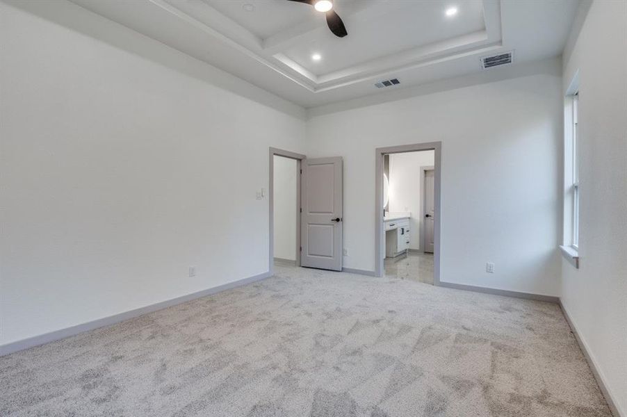 Unfurnished bedroom featuring light carpet, ensuite bath, a tray ceiling, ceiling fan, and a high ceiling