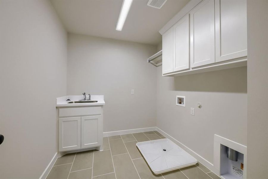 Laundry room featuring a utility sink with white cabinetry, tile flooring, overhead white cabinetry, and a clothing rod