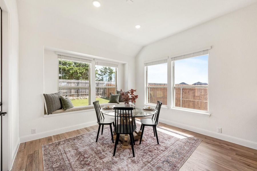 Bright dining nook with round glass table, black chairs, window bench seat, and hardwood floors