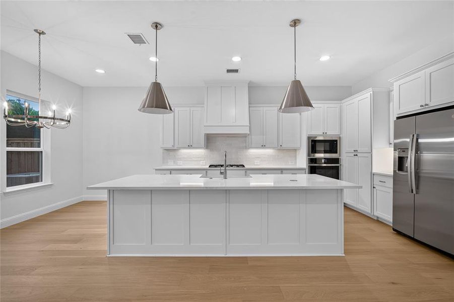 Kitchen featuring a large central island with a sink, white shaker cabinetry, stainless steel appliances, and wood-finish flooring Kitchen featuring a large central island with a sink, white shaker cabinetry, stainless steel appliances, and wood-finish flooring