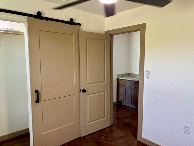 Unfurnished bedroom with concrete floors, a barn door, and connected bathroom
