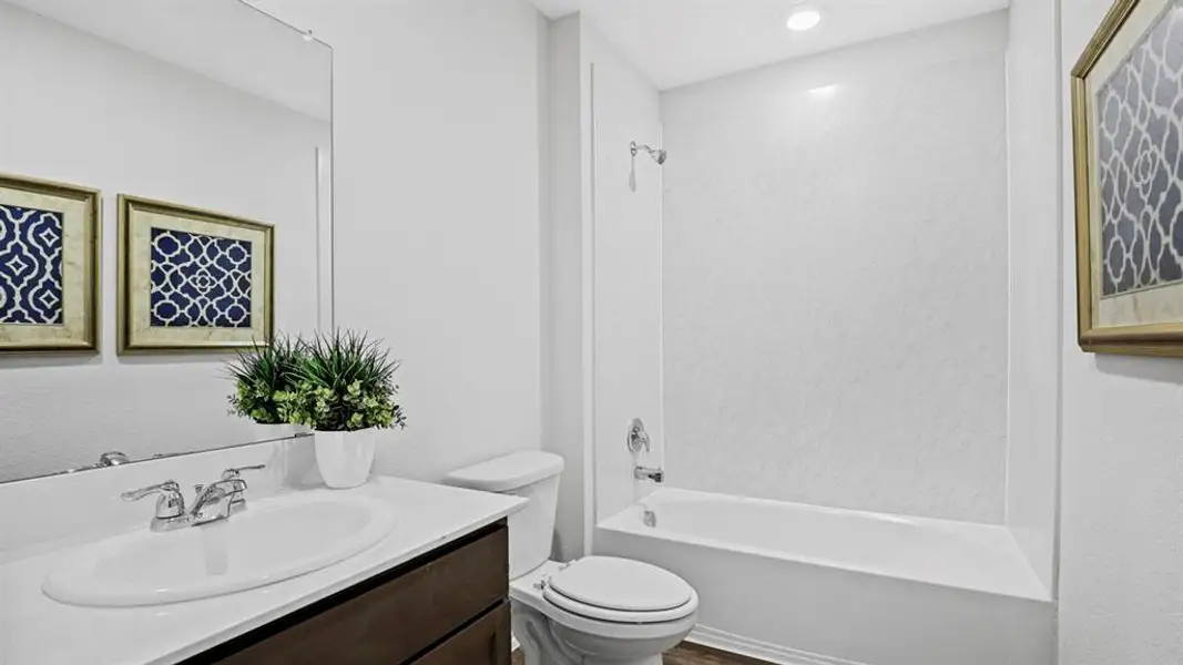 Bathroom featuring a white tub-shower combination, a vanity with an integrated sink and chrome faucet, and wood-finish flooring