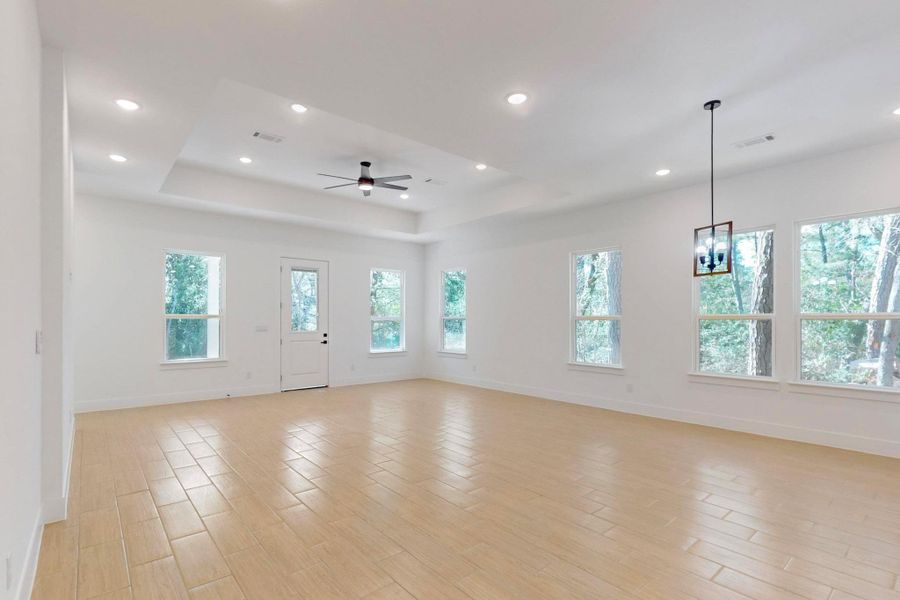 Unfurnished living room with a tray ceiling, wood tiled floors, a ceiling fan, and recessed lighting