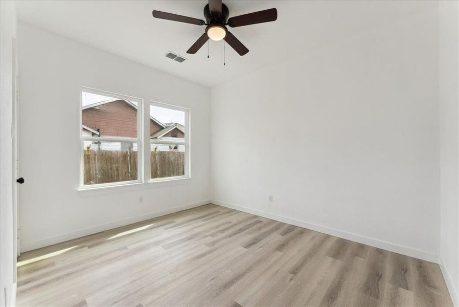 Spare room with baseboards, a ceiling fan, visible vents, and light wood-style floors