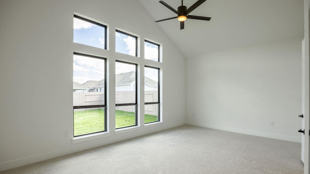 Unfurnished room featuring healthy amount of natural light, high vaulted ceiling, carpet flooring, and ceiling fan Unfurnished room featuring healthy amount of natural light, high vaulted ceiling, carpet flooring, and ceiling fan