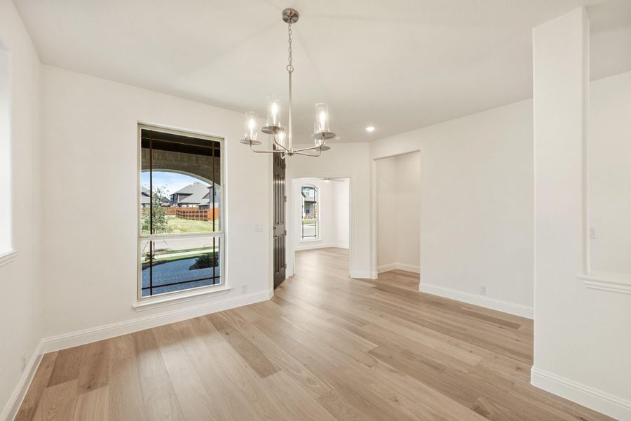 Empty dining room with light wood floors, white walls, and a modern chandelier Empty dining room with light wood floors, white walls, and a modern chandelier