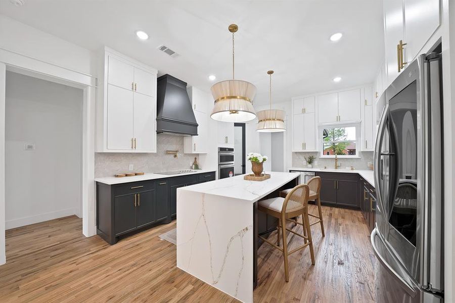 The kitchen features hardwood floors, a large island with a waterfall edge countertop, and two-tone cabinetry with gold hardware