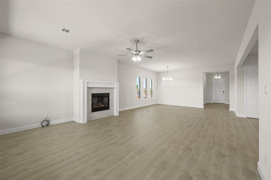 Unfurnished living room featuring a ceiling fan, a glass covered fireplace, light wood-type flooring, and a chandelier