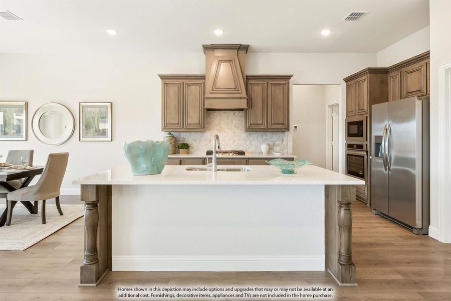 Kitchen with large center island, tan wood cabinets, decorative range hood, stone backsplash, and stainless steel appliances Kitchen with large center island, tan wood cabinets, decorative range hood, stone backsplash, and stainless steel appliances