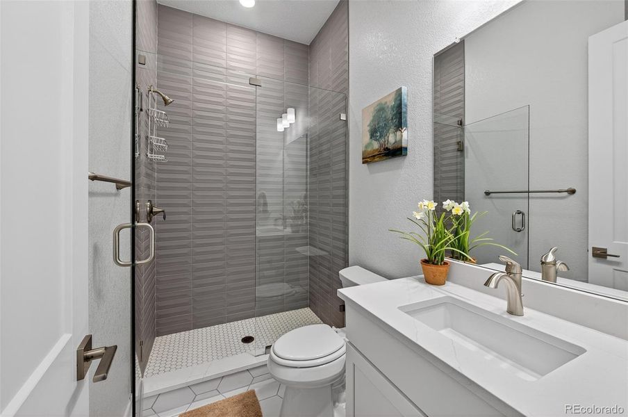 Guest Bathroom (Shower View) – Stylish full bath offering a sleek walk-in shower with geometric tile surround, modern fixtures, and a quartz-topped vanity.