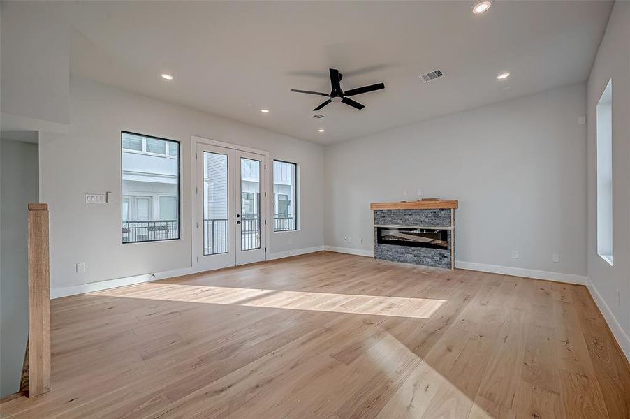 This spacious living room features hardwood floors, a modern fireplace, and ample natural light from large windows and glass doors. The ceiling fan and recessed lighting add to the contemporary feel. A walk-out balcony to step out.