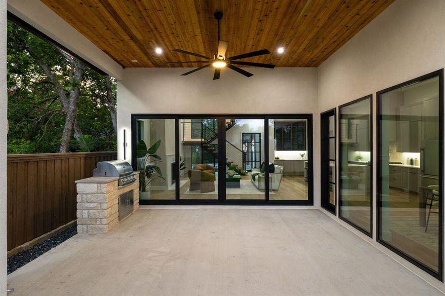 Expansive covered patio featuring a cedar plank ceiling with a ceiling fan, a built-in stone grill station, and a concrete floor