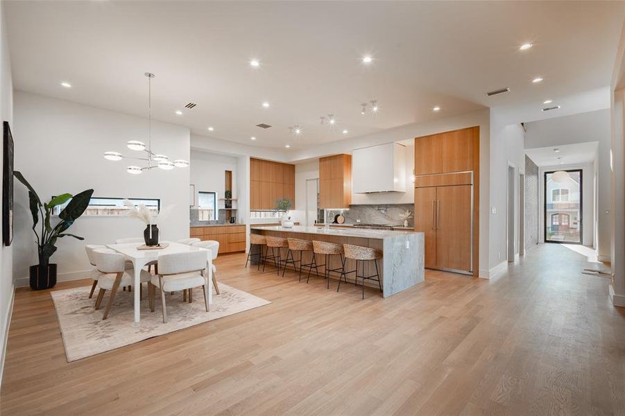 Kitchen featuring a kitchen bar, hanging light fixtures, an island with sink, paneled fridge, and light hardwood / wood-style floors