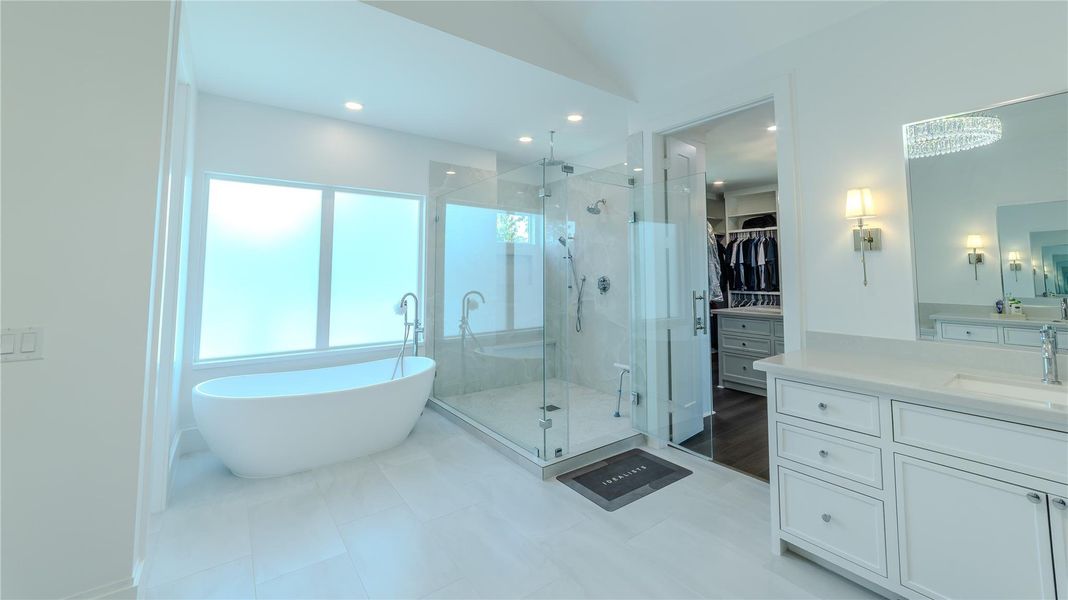 This spacious bathroom features a modern freestanding tub, a large glass-enclosed shower, and a dual-sink vanity with ample storage. It has bright natural light and a walk-in closet with built-in shelving.