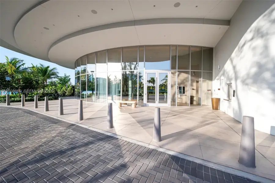 Curved floor-to-ceiling glass facade featuring an expansive covered porte-cochère, large-format tile flooring, and integrated recessed ceiling lighting