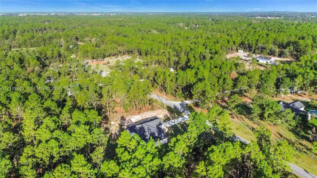 Aerial perspective of a property featuring a dense wooded lot, paved access road, and proximity to surrounding forest land